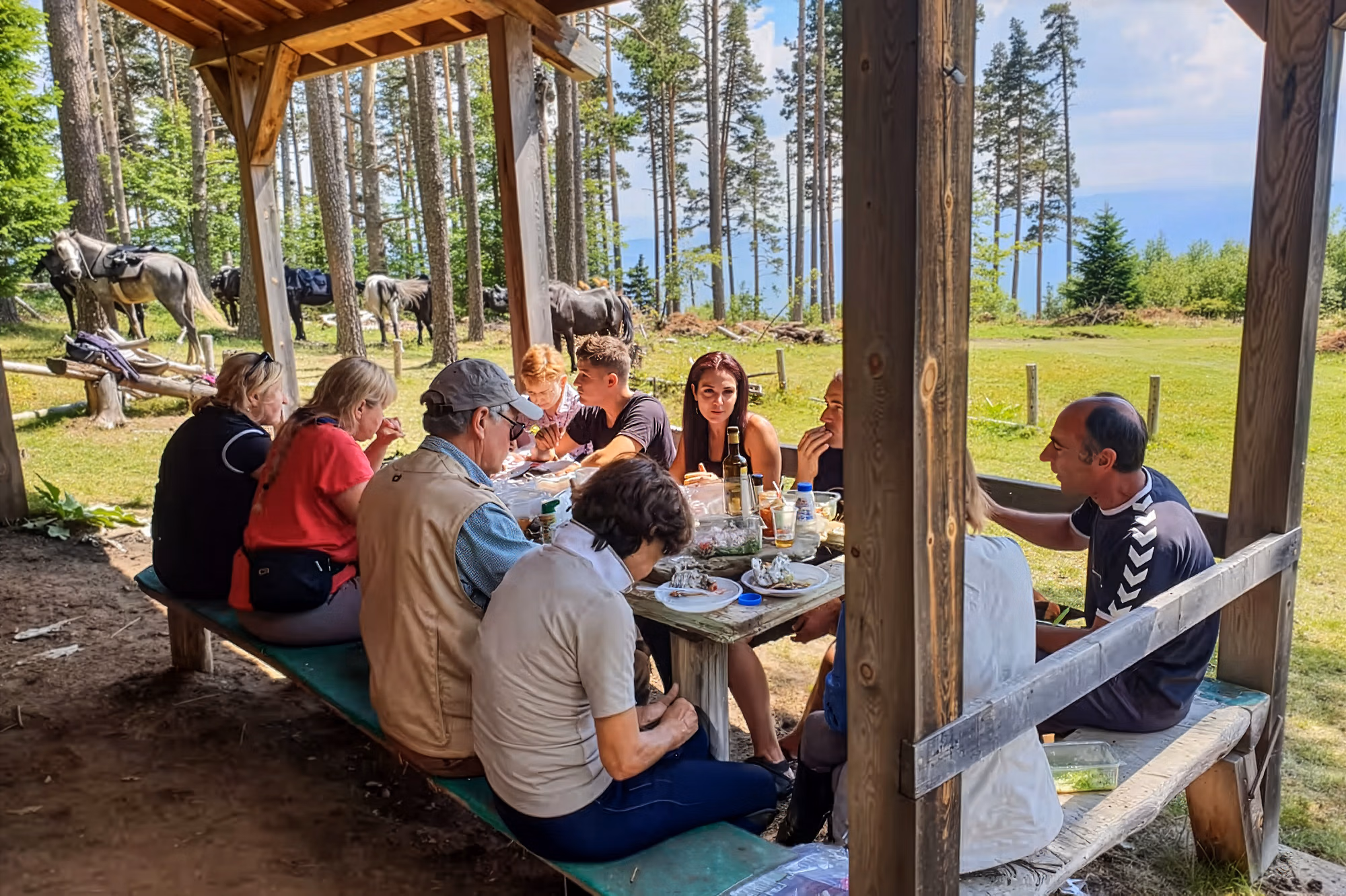 Un groupe de cavaliers se retrouve pour déjeuner autour d’une table dressée sous un abri rustique en bois dans les montagnes des Rhodopes.