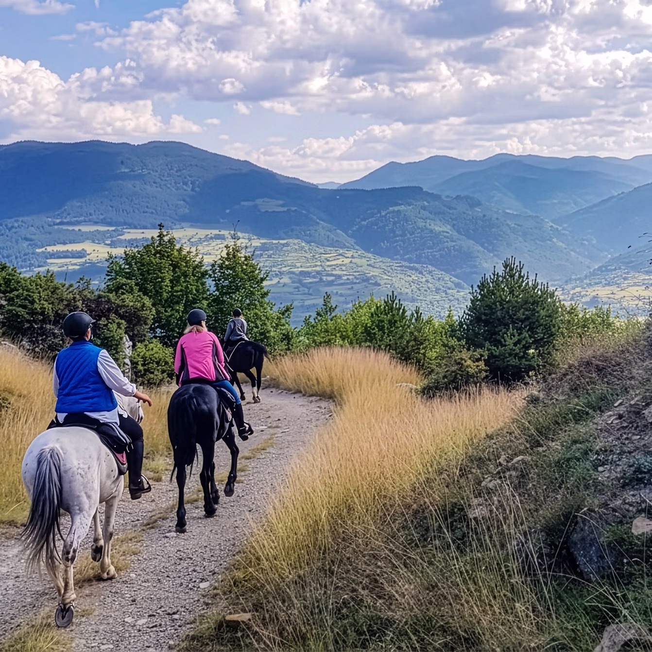 Un groupe de cavaliers descend une pente douce le long d’une imposante paroi rocheuse.