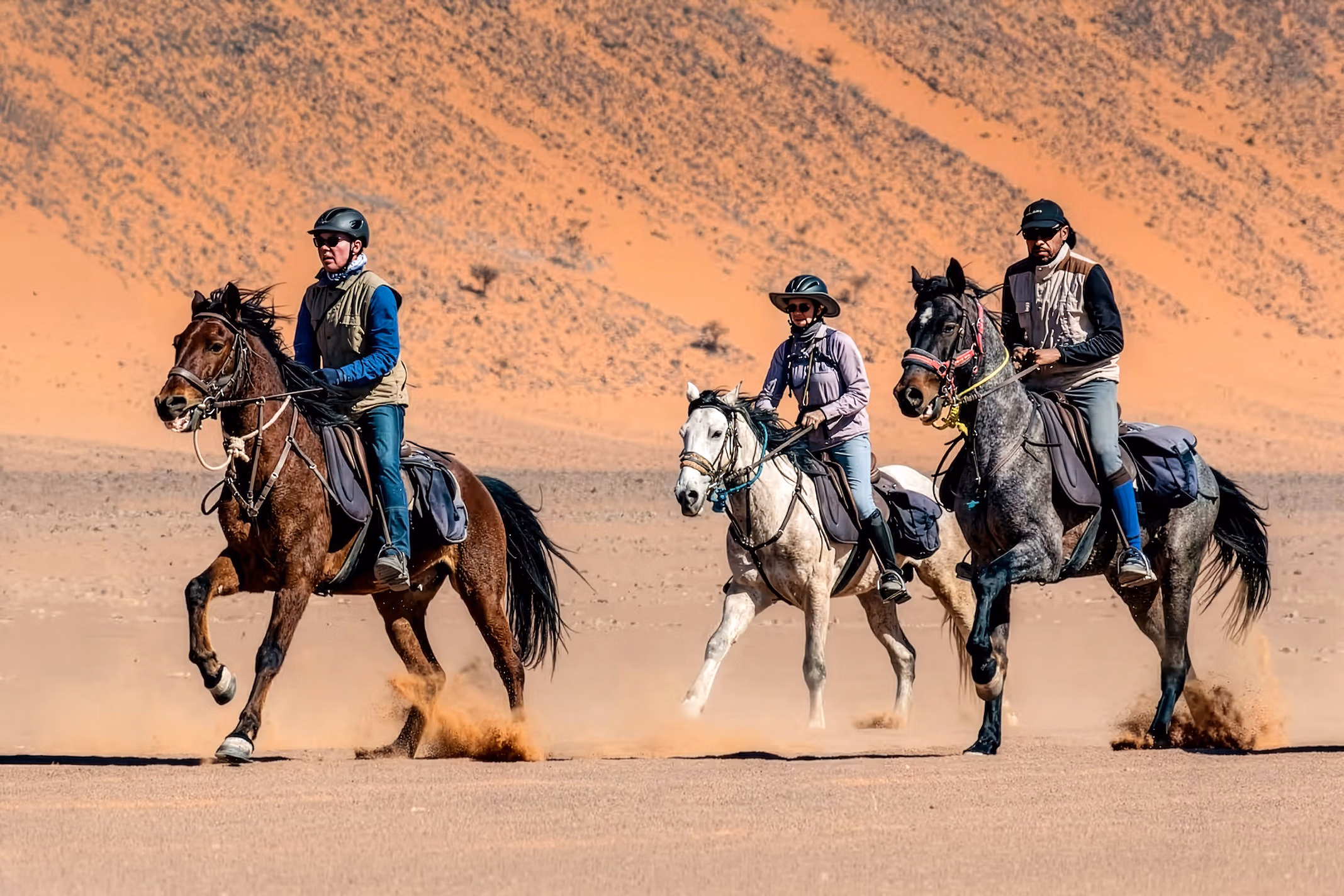 Trois cavaliers galopent à travers les vastes dunes du Sahara marocain.