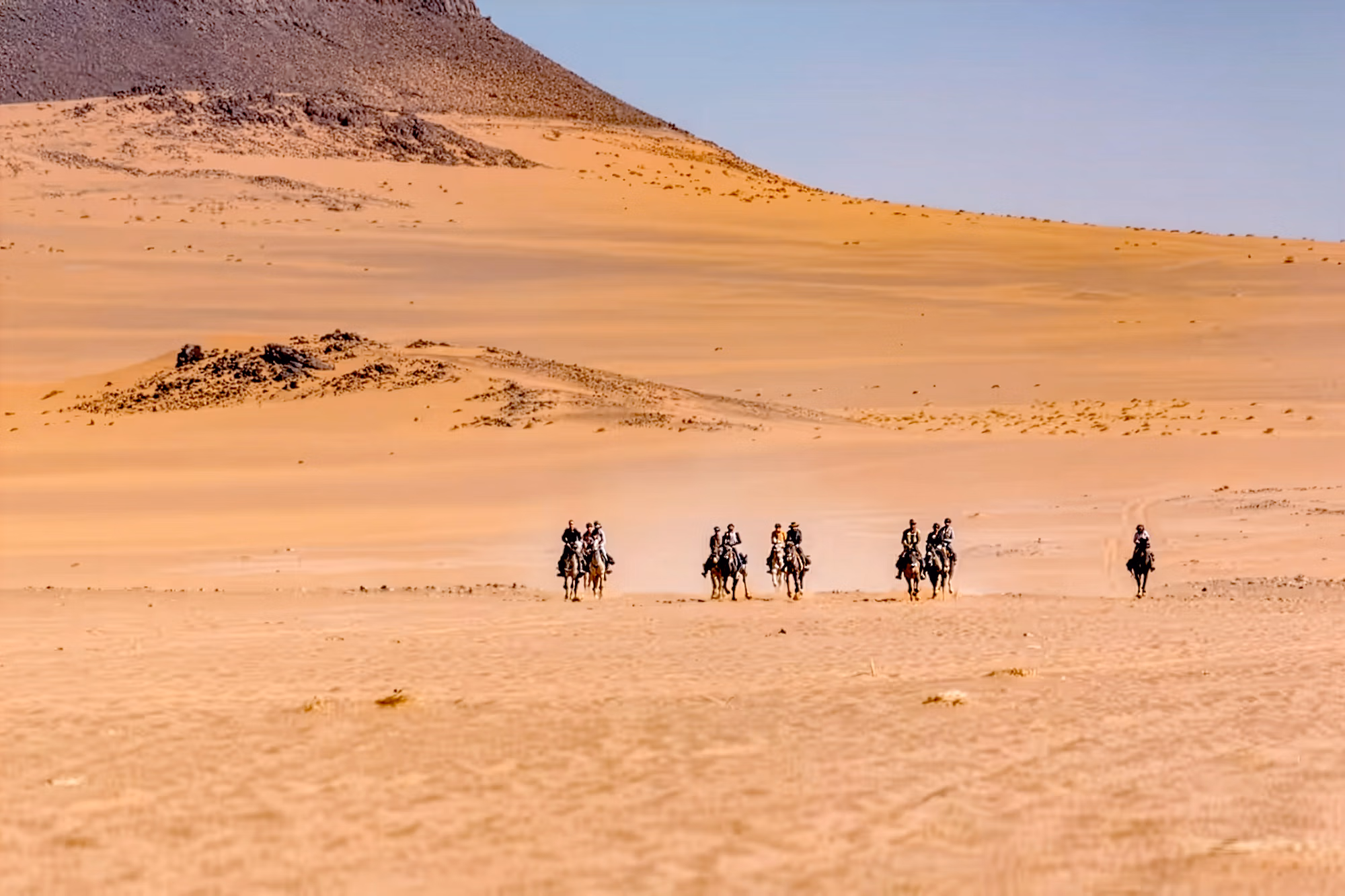 Vue panoramique du Sahara marocain avec un petit groupe de cavaliers au loin galopant vers l’objectif.