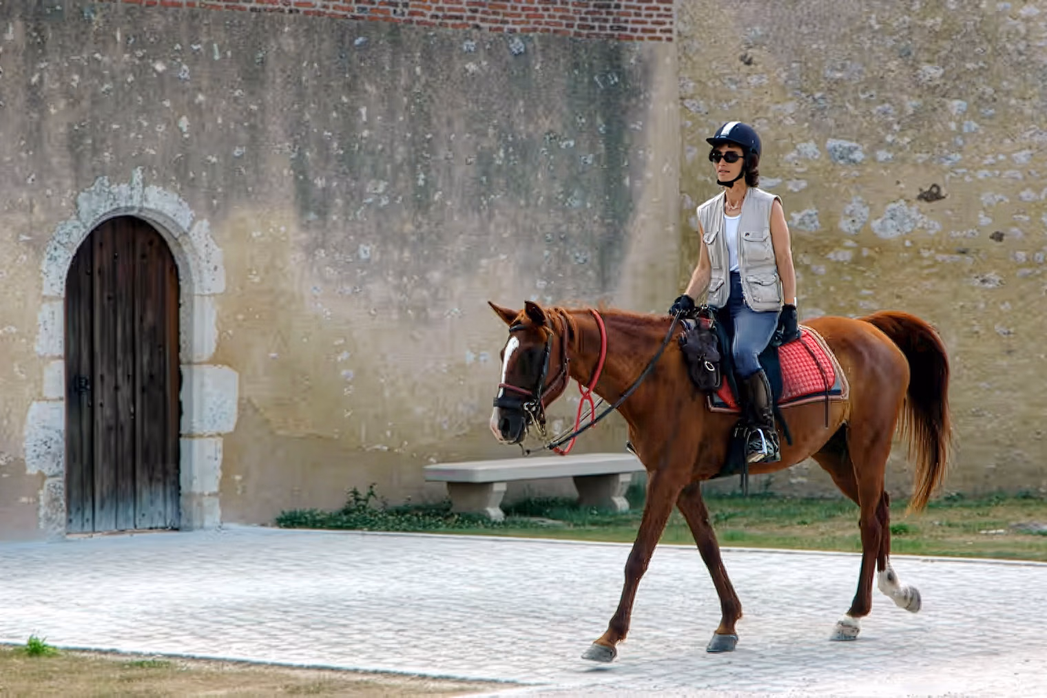 Une cavalière traverse à cheval la cour historique en pierre d’un domaine traditionnel français.