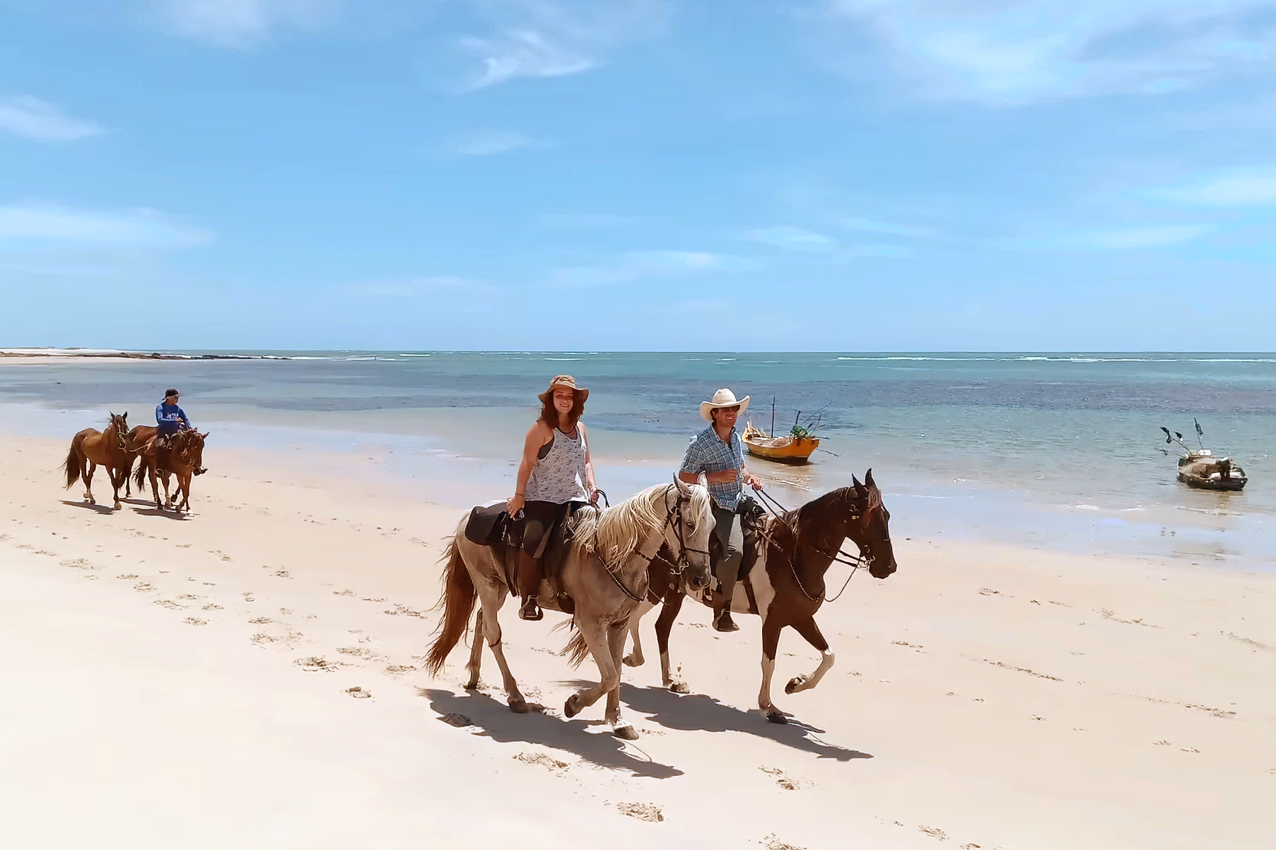 Un petit groupe de cavaliers explore une vaste plage tropicale déserte.