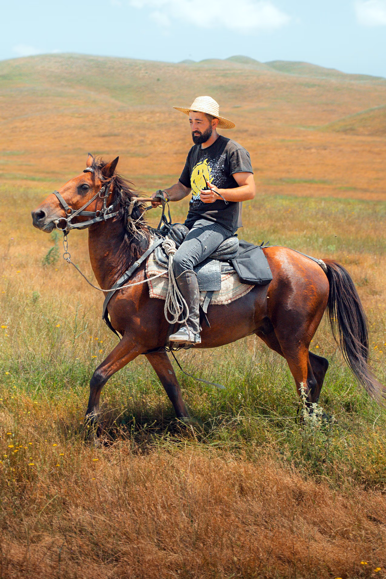 Un homme à cheval traverse des champs d’herbes sèches et brunes, avec une zone de végétation plus verte en contraste.