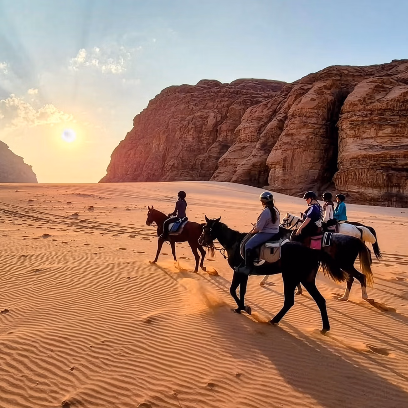 Un groupe de cavaliers se dirige vers le coucher du soleil dans le désert, le long de falaises de grès rouge.