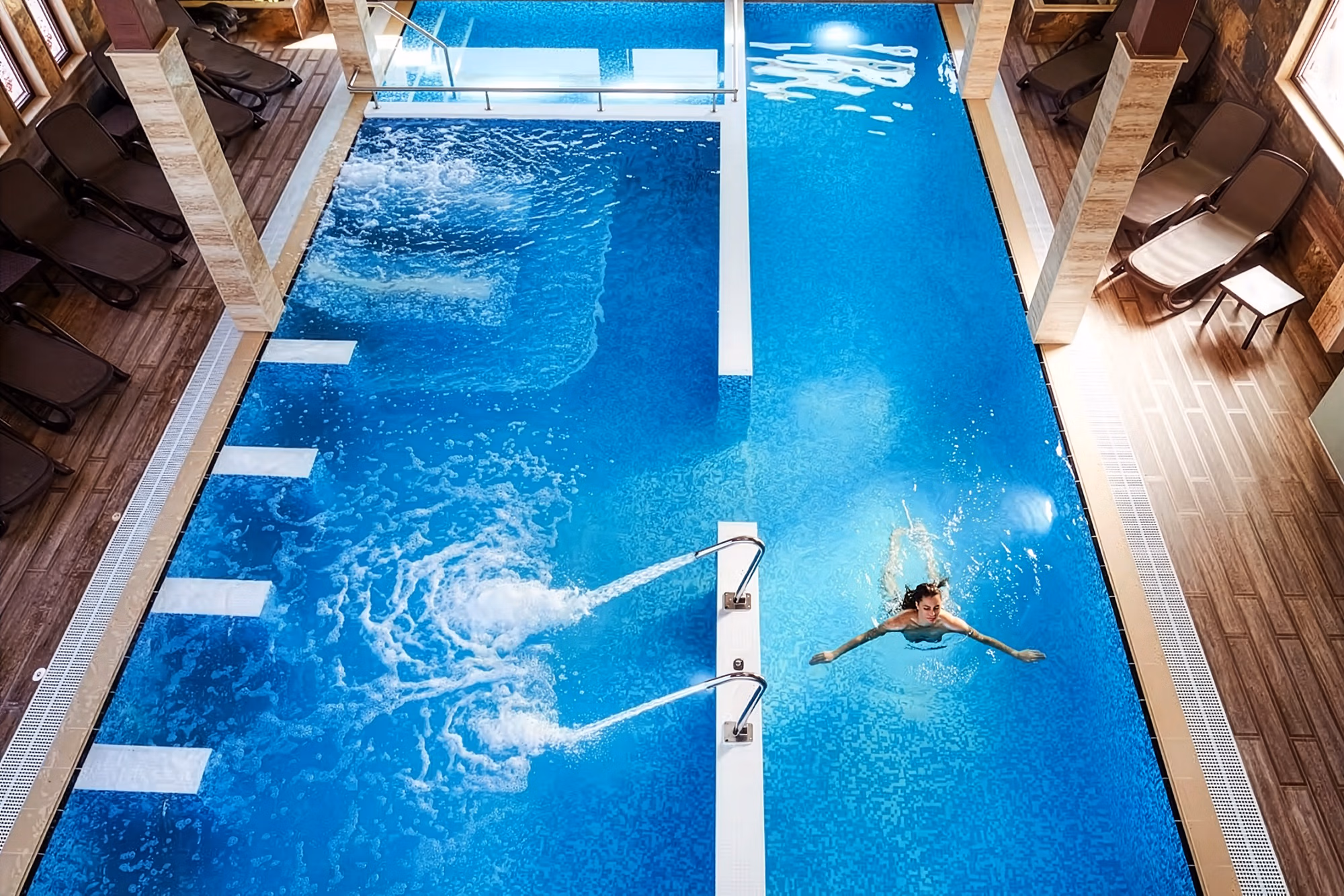 Une femme nageant dans une piscine intérieure moderne d’un complexe de bien-être haut de gamme en Bulgarie, vue directement du dessus.