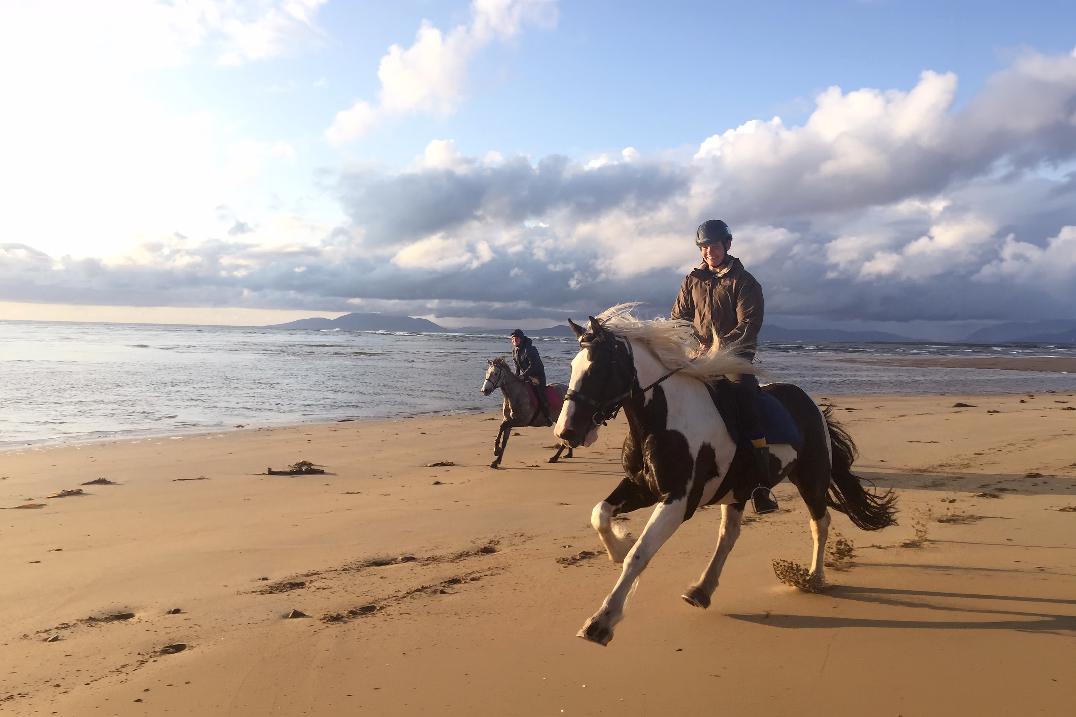 Deux cavaliers souriants lancés au grand galop sur une immense plage