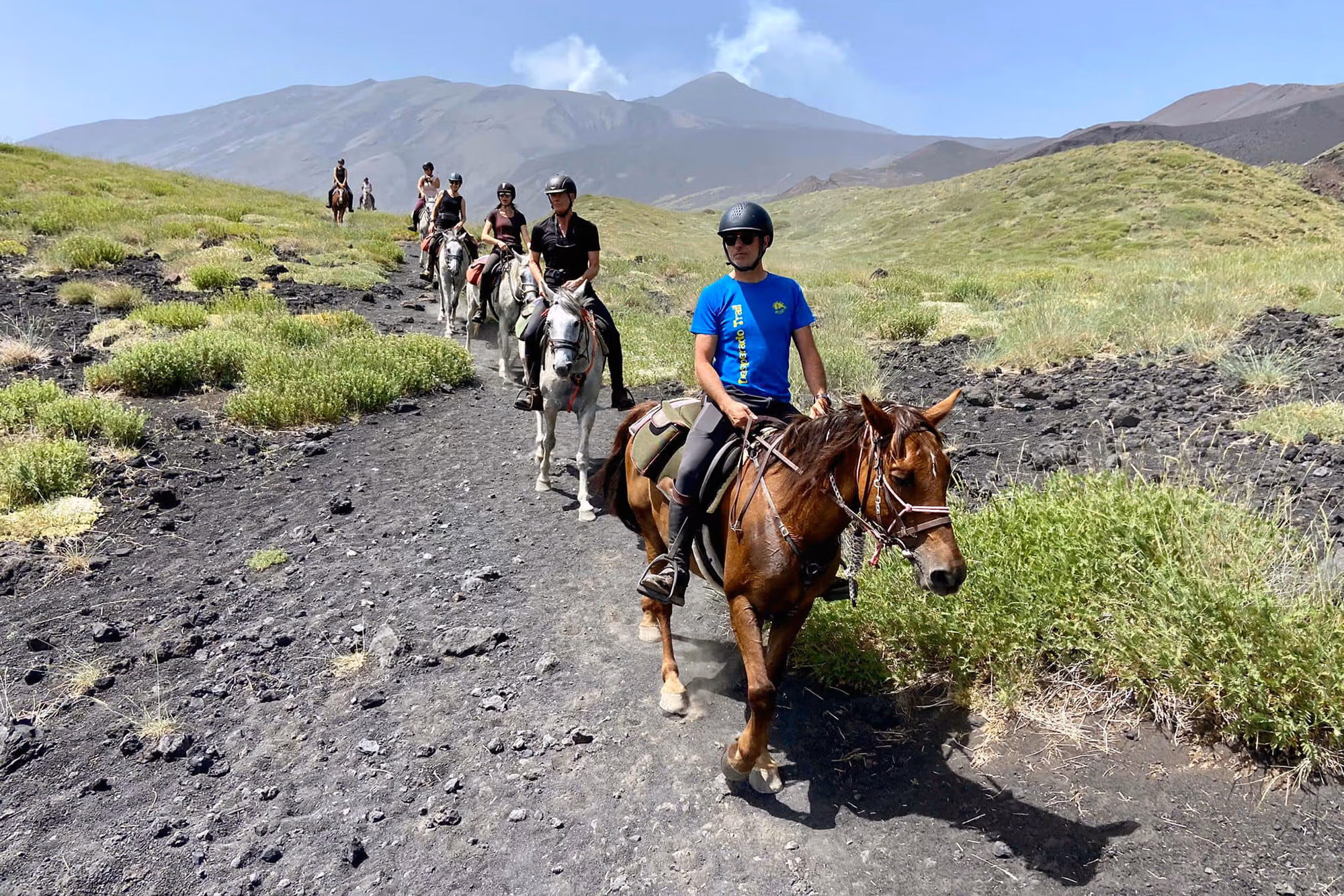 Une file de cavaliers suit son guide à travers un paysage volcanique de lave près de l’Etna, en Sicile.