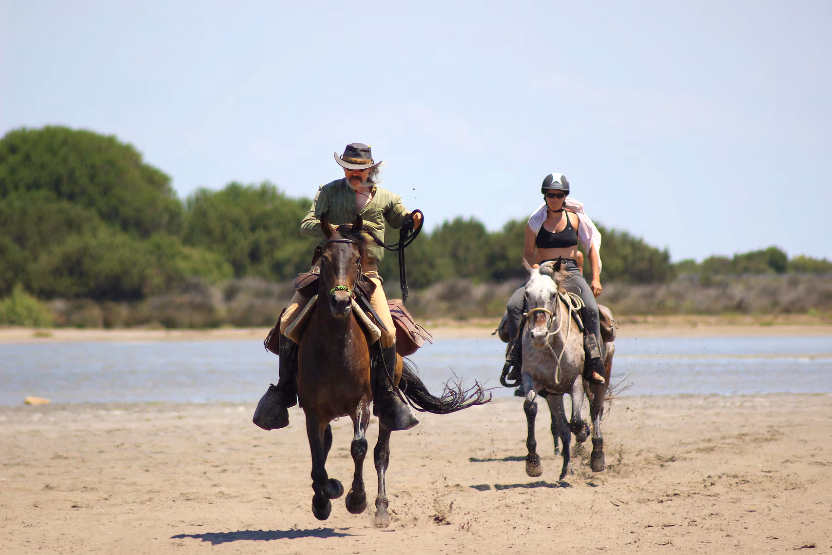 Un guide a cheval et un cavalier chevauchent sur une plage de sable de Camargue face caméra