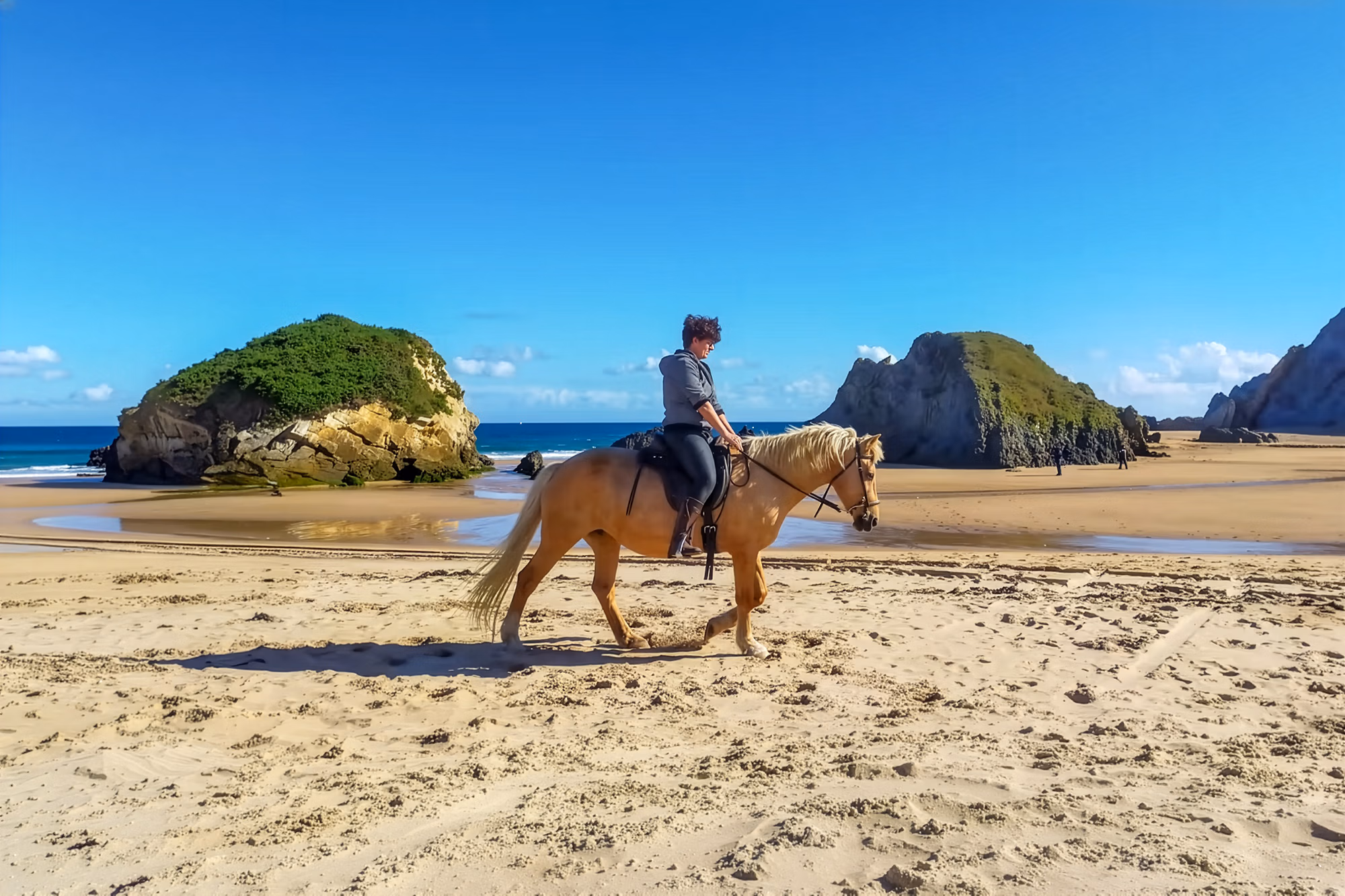 Un cavalier longe une grande plage de sable, avec de belles formations rocheuses dans la mer.