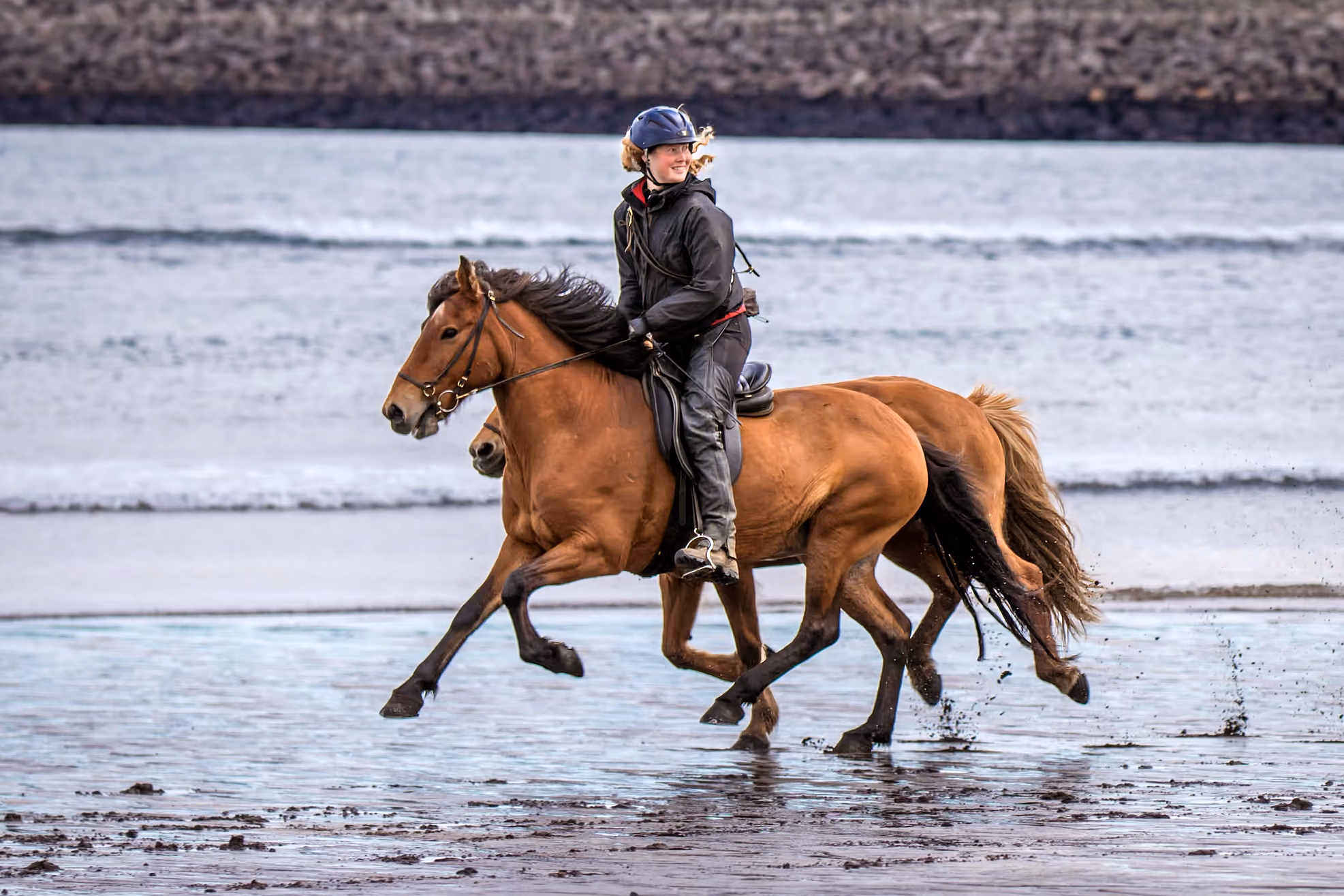 Cavalière sur un cheval islandais avançant rapidement dans l’eau lors d’une randonnée équestre entre rivières et paysages volcaniques en Islande.