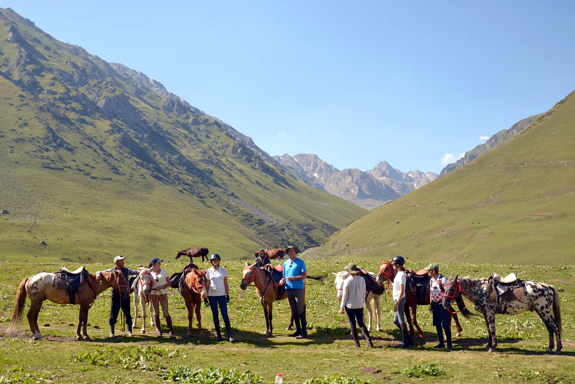 Un groupe de cavaliers au Kirghizistan pose fièrement aux côtés de leurs chevaux dans un vaste paysage d’un vert éclatant.