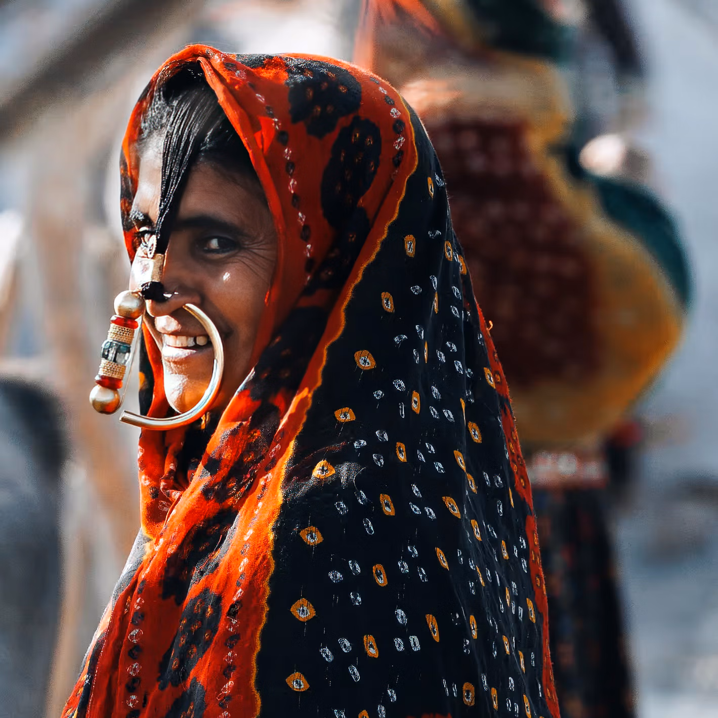 Portrait d’une femme souriante en tenue traditionnelle colorée, portant un grand anneau de nez rond.