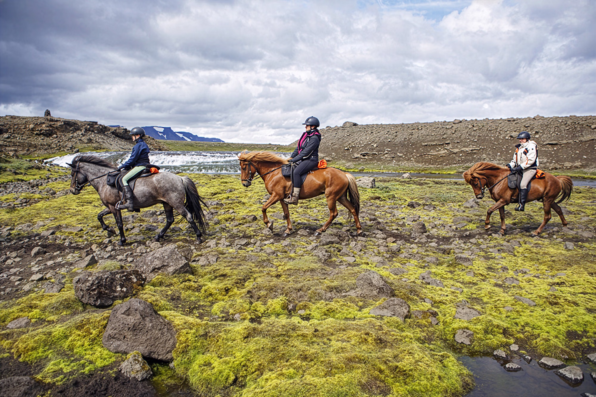 Groupe de cavaliers traversant les grands espaces volcaniques sur des chevaux islandais pendant un séjour équestre en Islande.