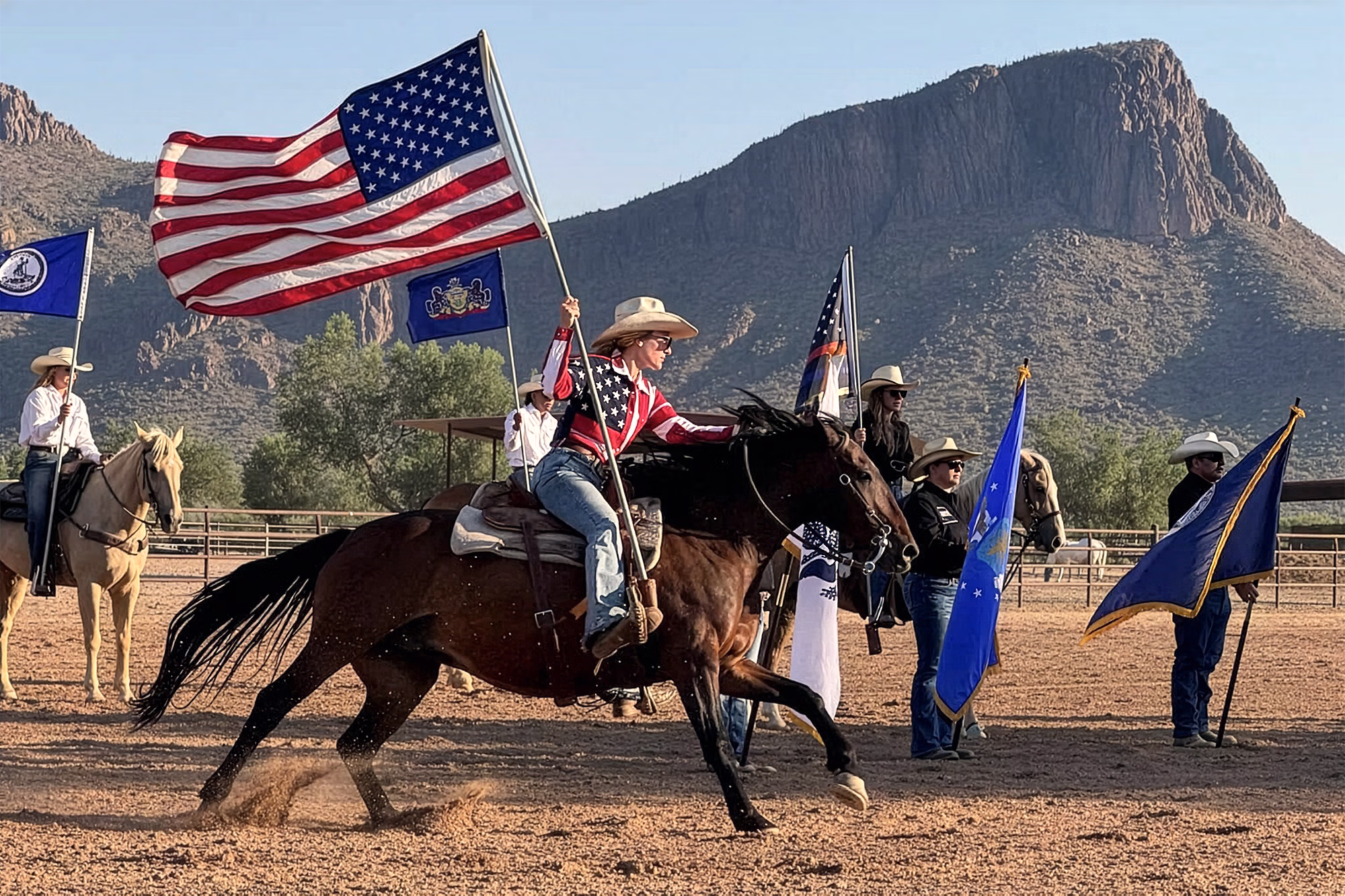 Une cow-girl galope à vive allure à cheval à travers un pâturage du ranch en brandissant fièrement un grand drapeau américain.
