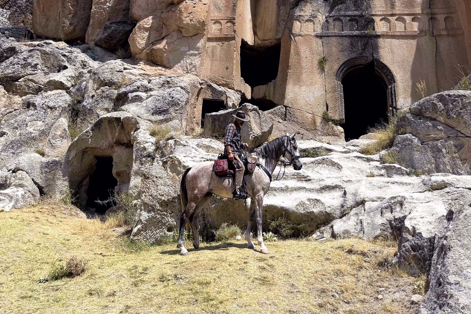 Un cavalier à cheval devant d’anciennes habitations troglodytes creusées dans la roche en Cappadoce, en Turquie.