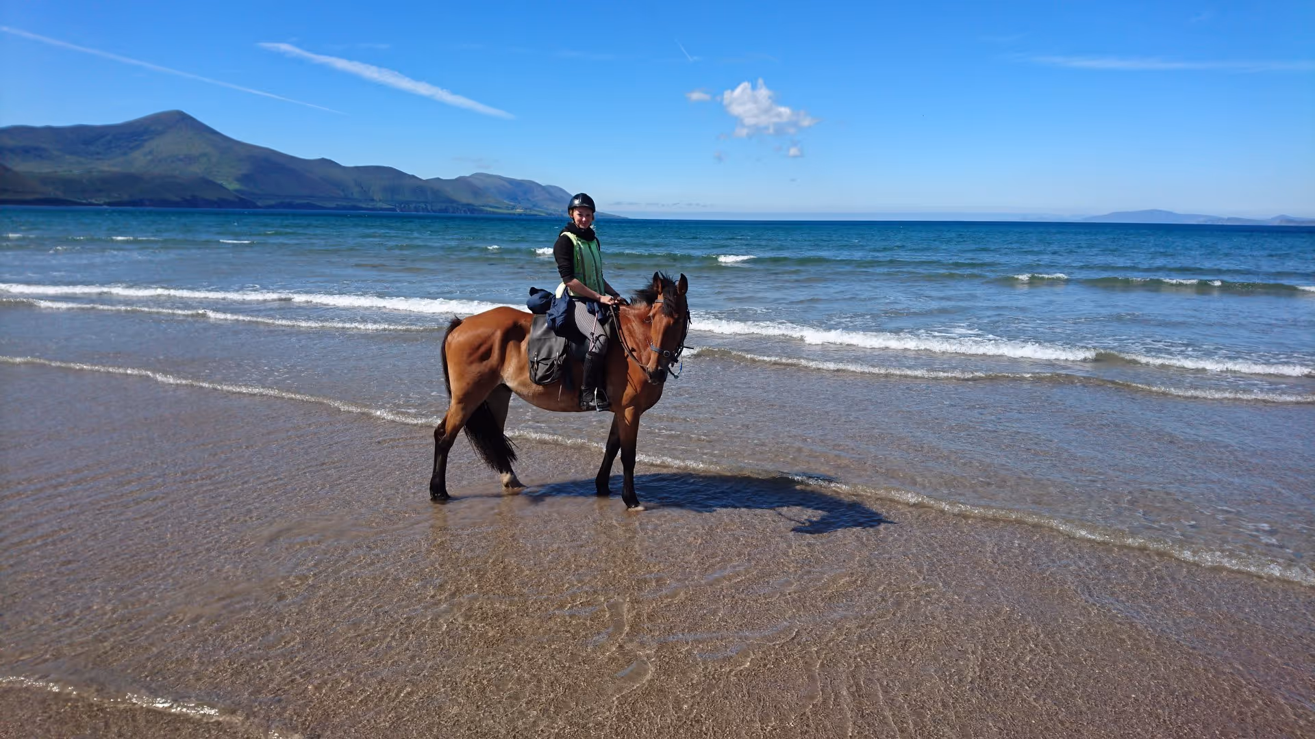 Un cavalier a cheval regarde la caméra sur une belle plage en Irlande, sous un beau ciel bleu.