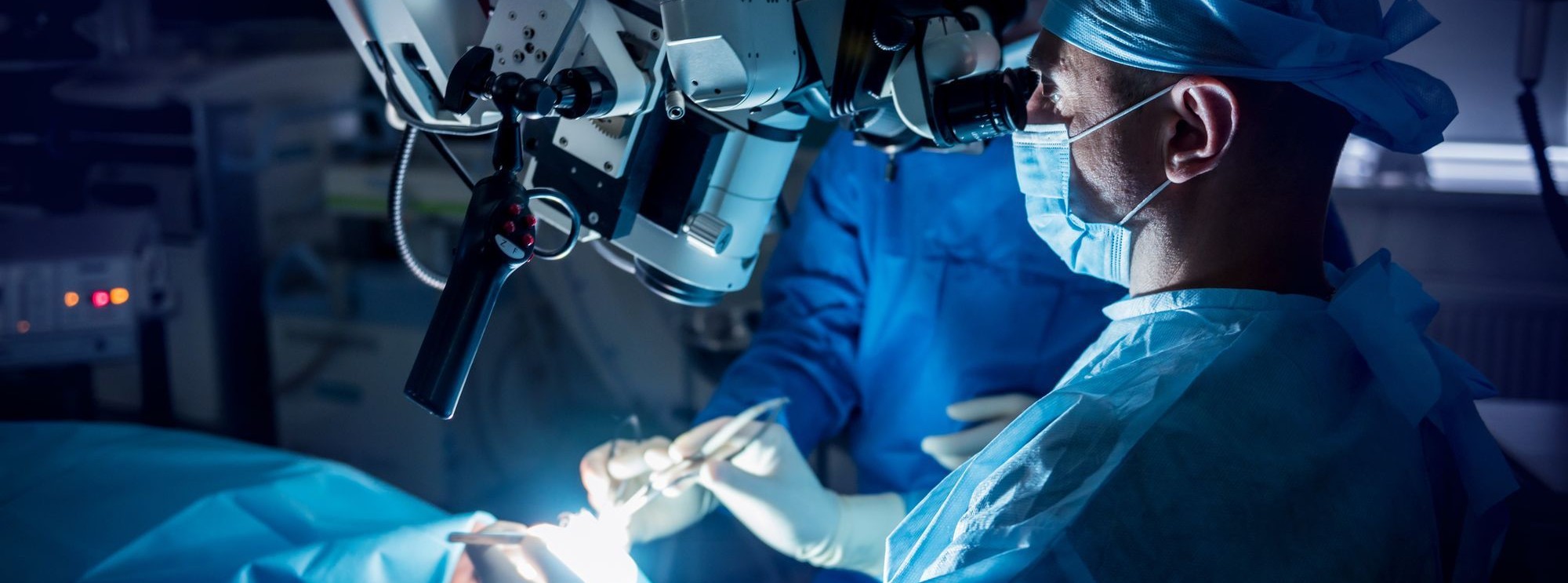 Cardiac catheterization lab team performing a coronary angioplasty, with live fluoroscopic images of the heart displayed on a large monitor overhead.