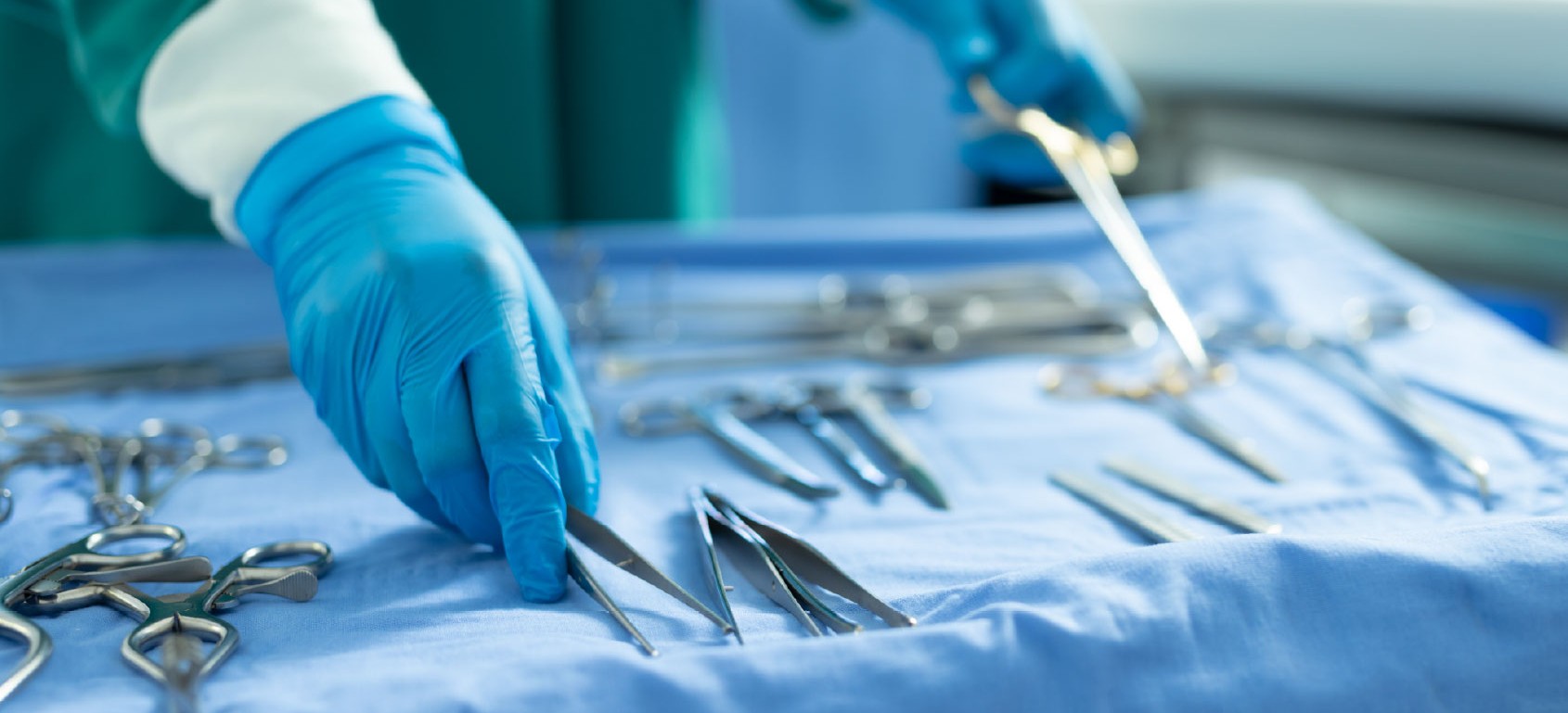Surgeon in blue scrubs and mask handling a catheter delivery device over a draped patient during an interventional procedure