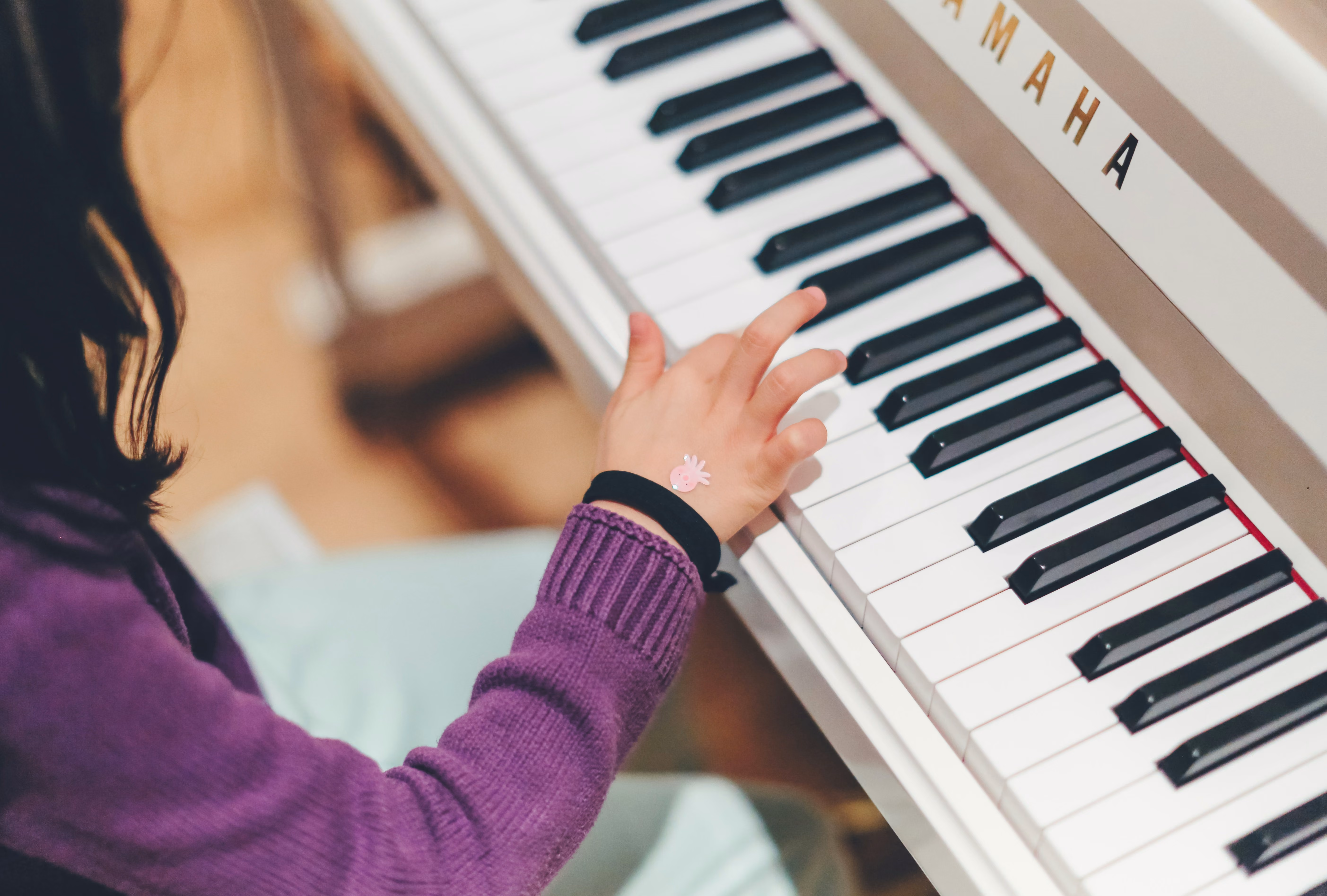 A young girls sits at the piano slowly figuring out how to play the keys with her right hand.