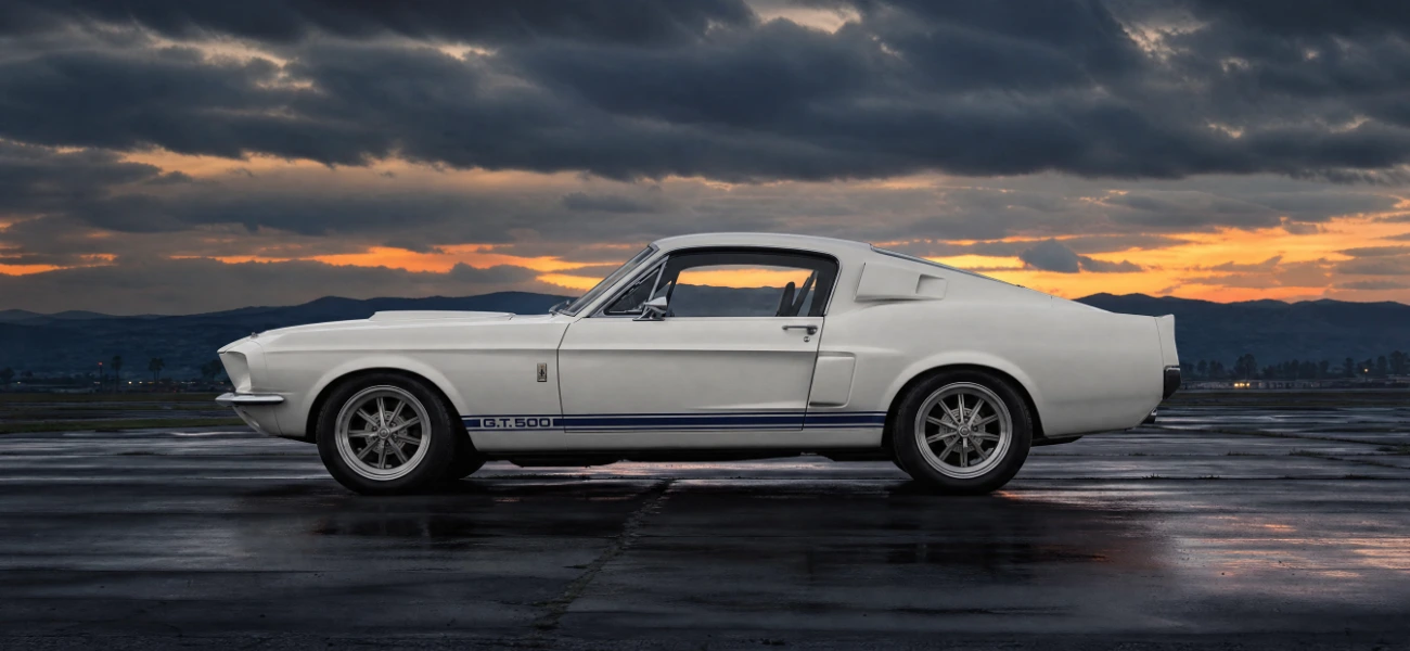 White 1967 Shelby GT500 Mustang with blue racing stripes at dusk, an American muscle car ready for appraisal