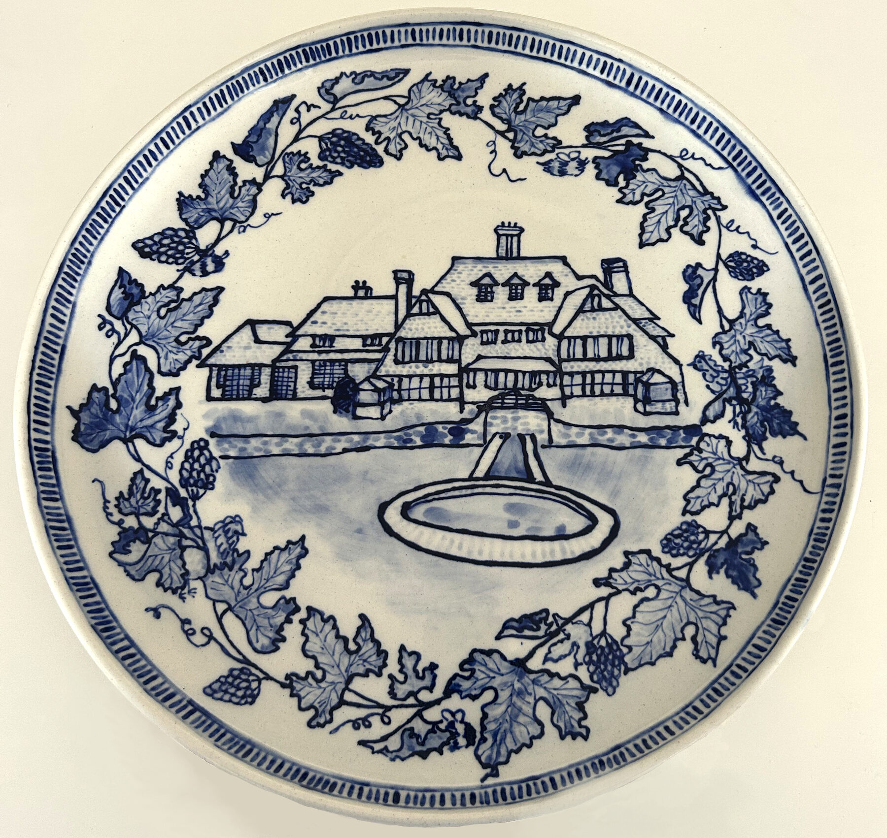 Hand-painted blue and white plate of a house framed with vines