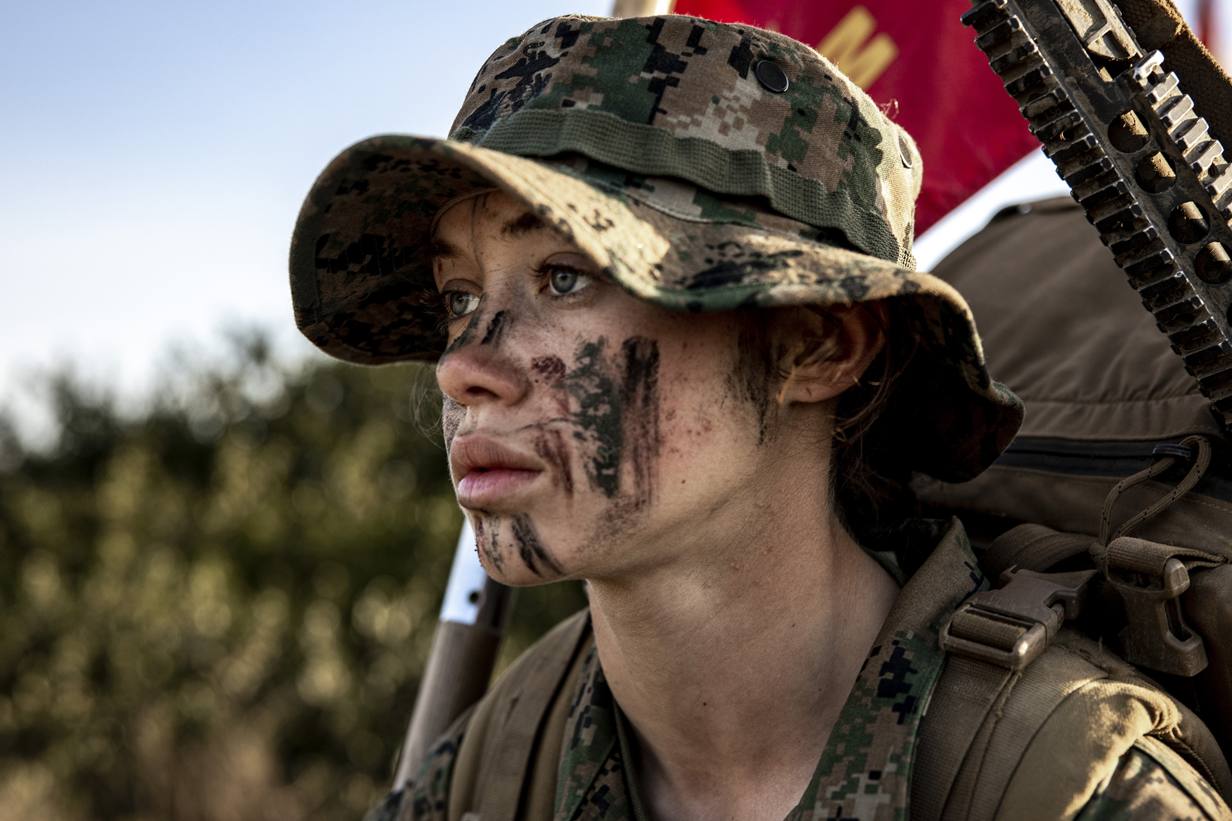 A woman who has mud on her face wears camo and a backpack.