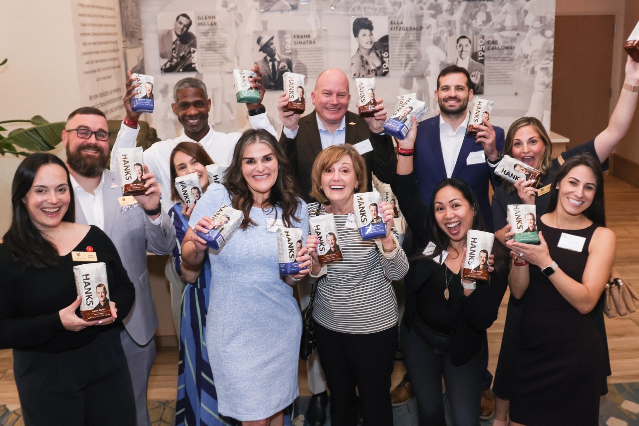 A group of people cheerfully holding up bags of Hanks coffee while posing together at an event.