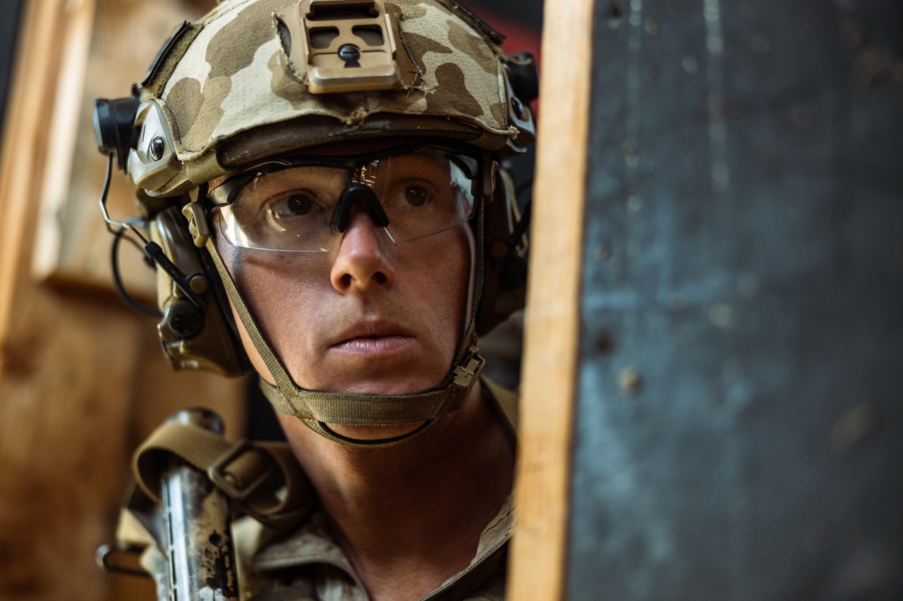 Close-up of a military service member in tactical gear, helmet, and protective glasses looking intent during training.