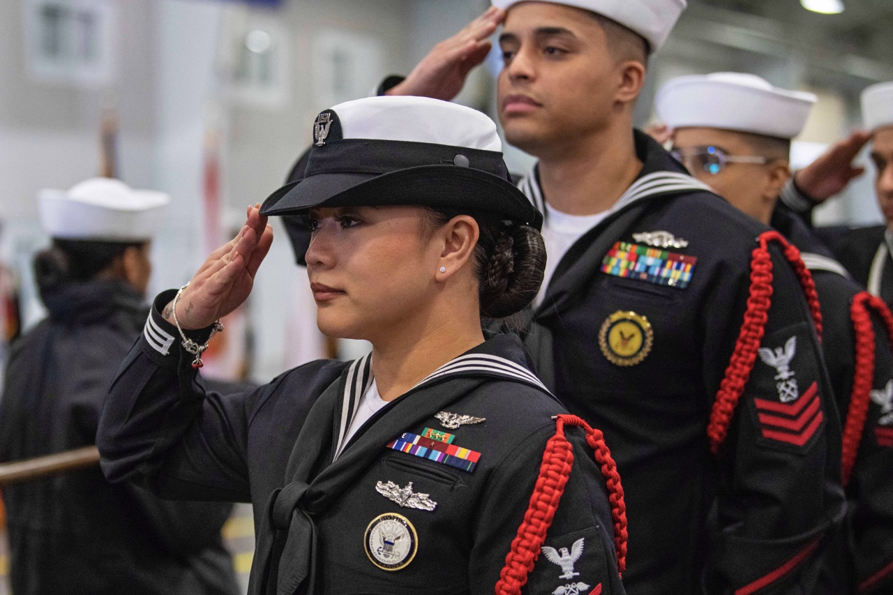 U.S. Navy sailors standing in formation and rendering a formal hand salute in dress uniform.
