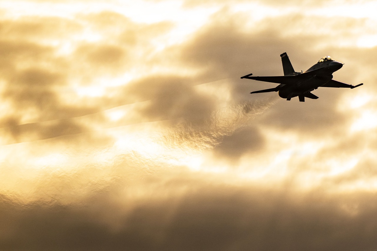 Silhouette of a fighter jet soaring through golden-lit clouds at sunset.