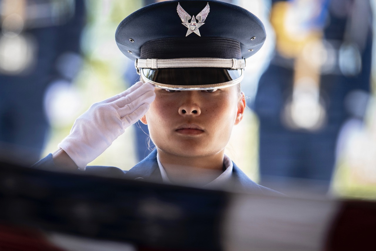 Close-up of an individual in uniform wearing a white glove and service cap, offering a formal salute.