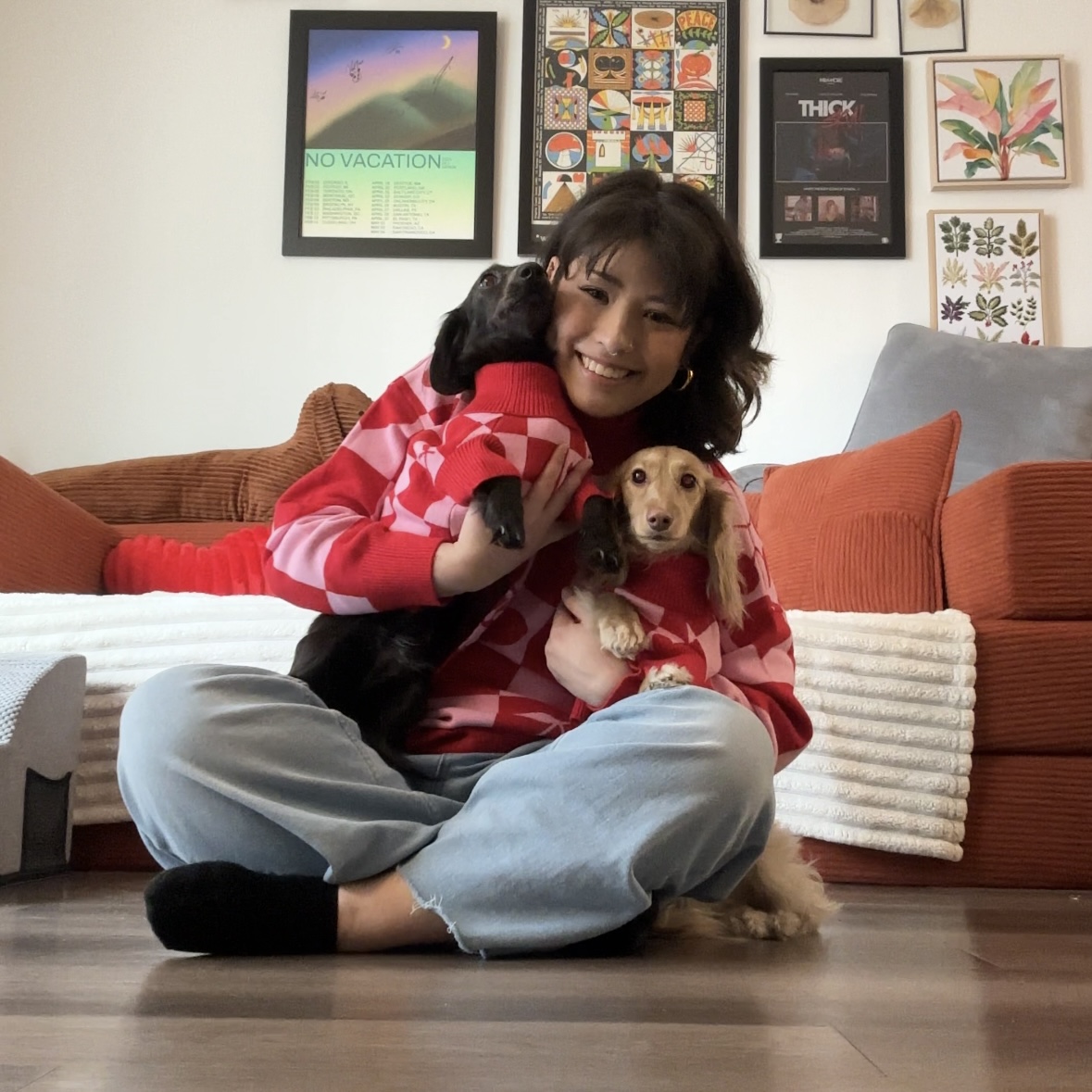 A young woman sitting on the floor holding two mini dachshunds.