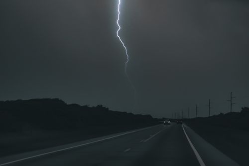 A bright lightning bolt cutting through a dark storm sky above a highway.