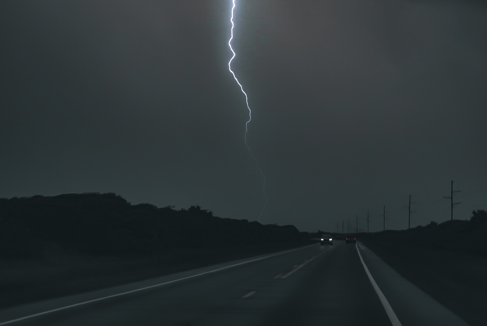A bright lightning bolt cutting through a dark storm sky above a highway.