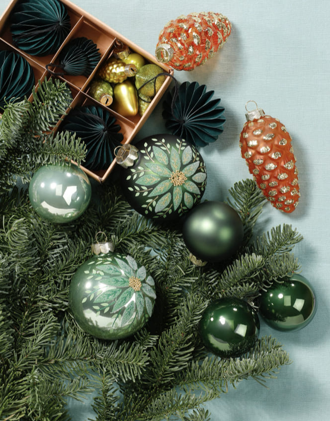 Grüner Christbaumschmuck mit Kugeln, Zapfen und Papierornamenten.