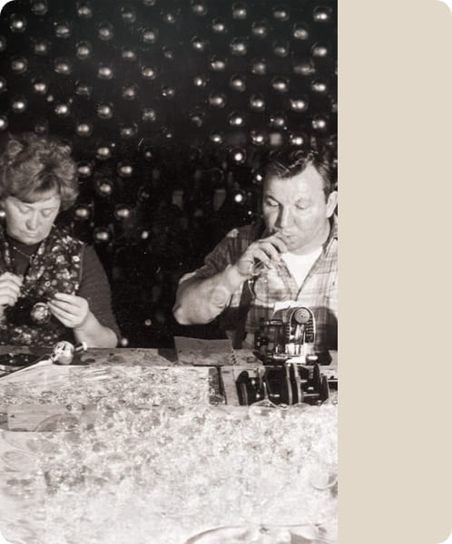 Historische Schwarzweißaufnahme zweier Menschen bei der Arbeit an Glasschmuck.