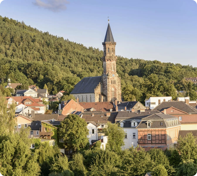 Blick über einen Ort mit Kirchturm und bewaldeten Hügeln.