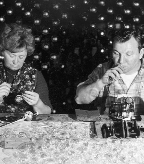 Historische Schwarzweißaufnahme zweier Menschen bei der Arbeit an Glasschmuck.