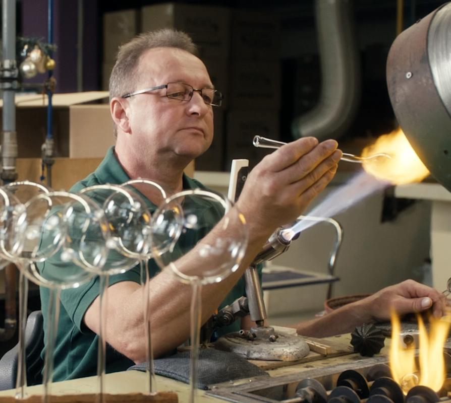 Ein Glasbläser formt erhitztes Glas vor einer Flamme.