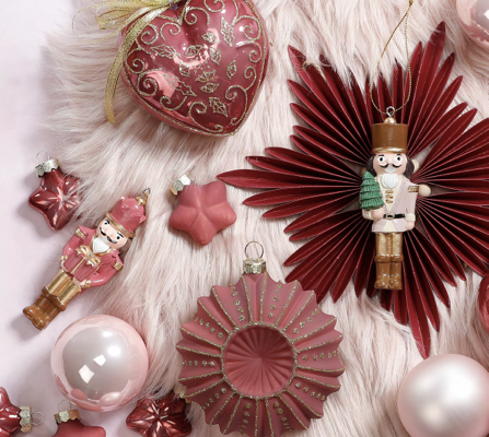 Rote und rosafarbene Weihnachtsdekoration mit Kugeln, Papiersternen und Nussknacker.