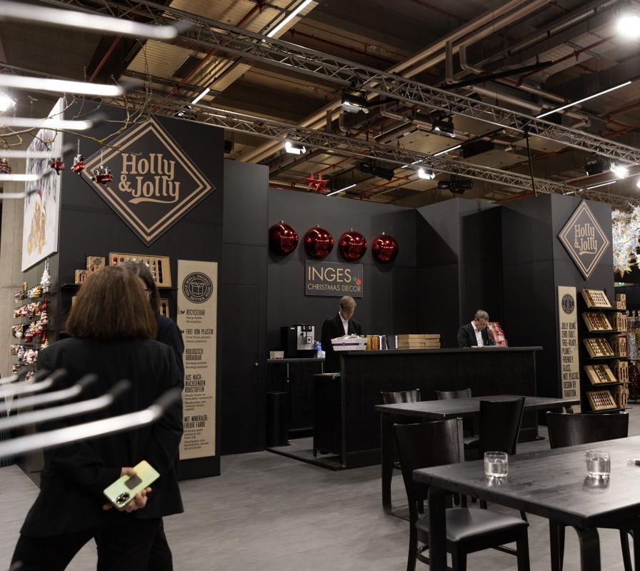 Messestand von Holly & Jolly mit dunklen Ausstellungswänden und Besprechungsbereich.