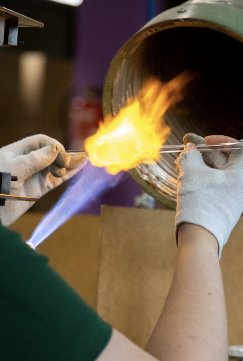 Glas wird von Hand vor einer offenen Flamme geformt.