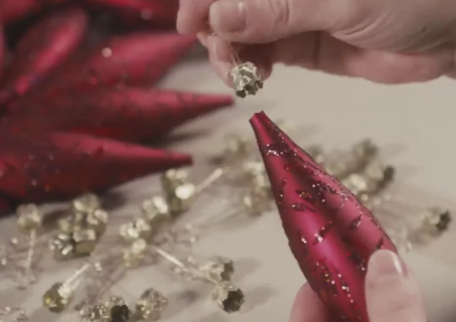 Ein Sternkrönchen wird auf ein rotes Glasornament gesetzt.