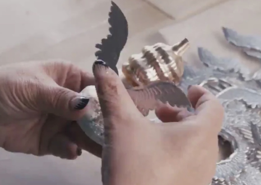Ein Glasornament in Tierform wird von Hand mit Flügeln ergänzt.
