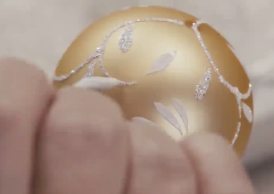 Ein goldenes Glasornament wird von Hand mit einem feinen Dekor versehen.