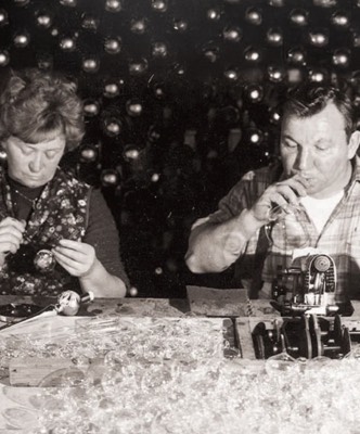 Historische Schwarzweißaufnahme zweier Menschen bei der Arbeit an Glasschmuck.