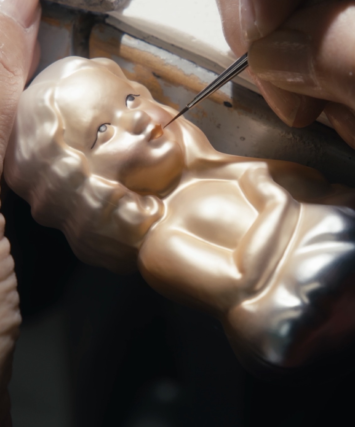 Ein Gesicht auf einem Glasornament wird mit einem feinen Pinsel bemalt.