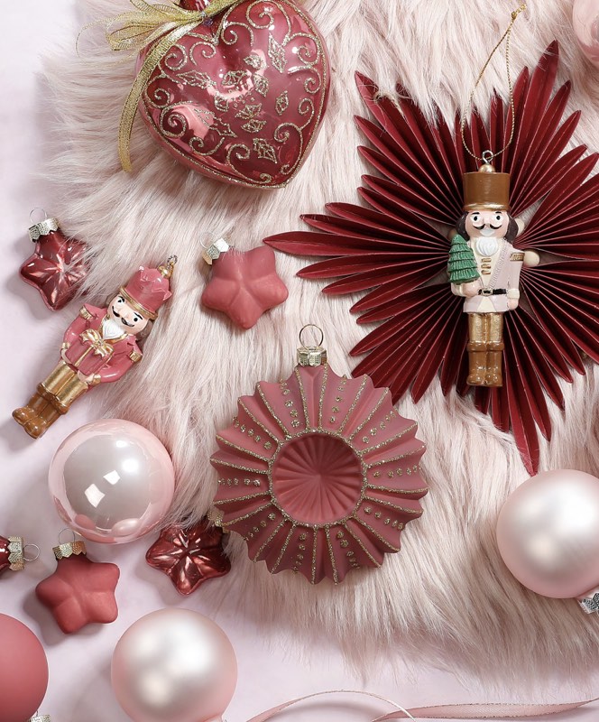 Rote und rosafarbene Weihnachtsdekoration mit Papiersternen, Kugeln und Nussknacker.