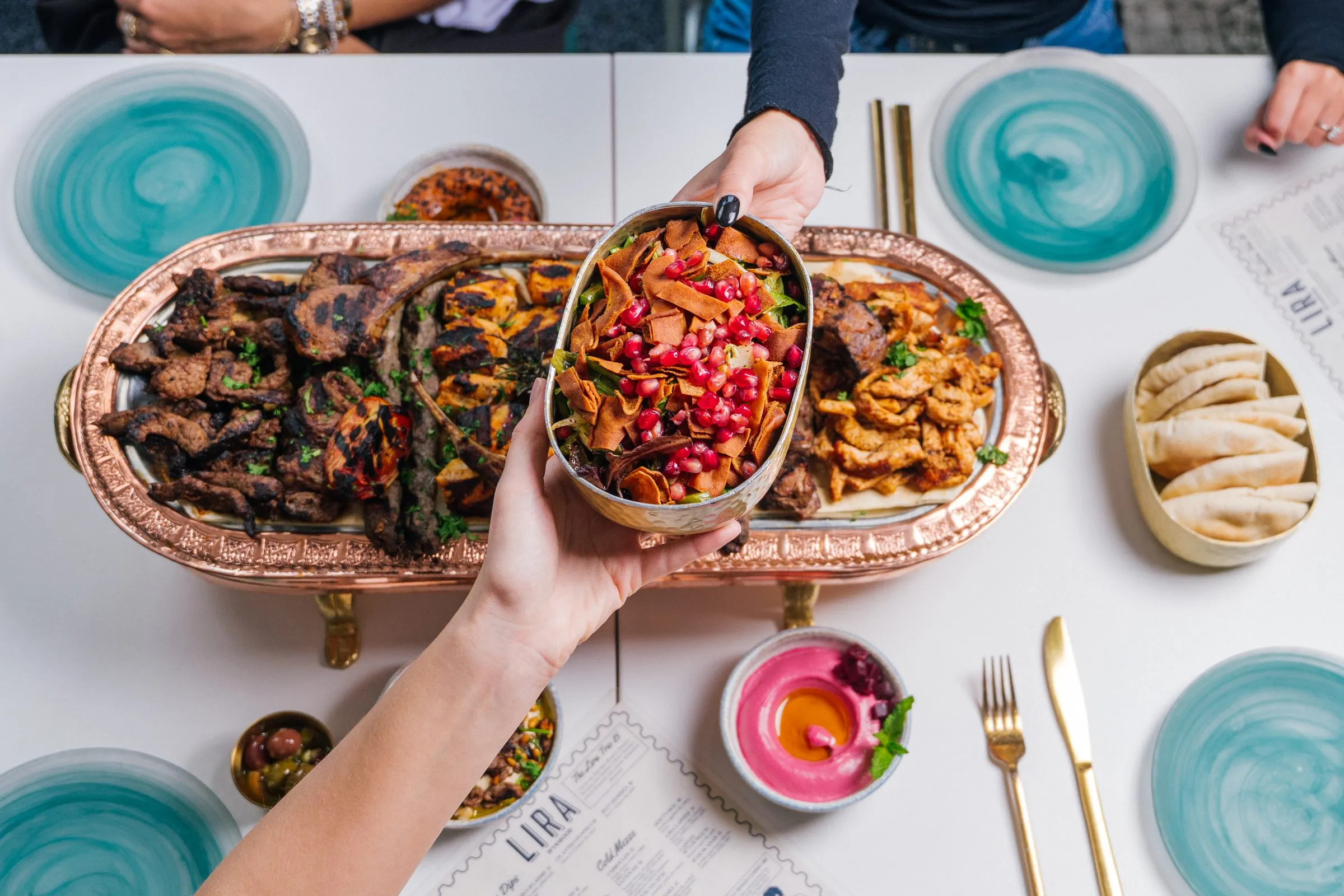 Overhead spread of Lira House mezze and grilled dishes on a copper tray.