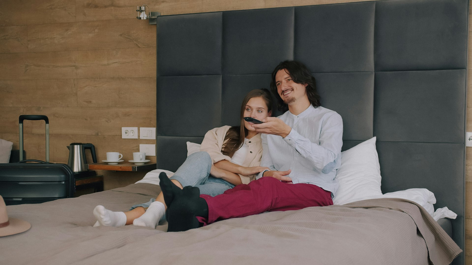 A couple sitting on a hotel bed watching television, illustrating connected TV advertising for hotels. Photo by Vitaly Gariev on Unsplash.